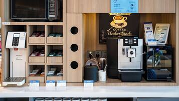 A coffee shop counter with a coffee machine, a hot water dispenser, and various tea and coffee products displayed on shelves.