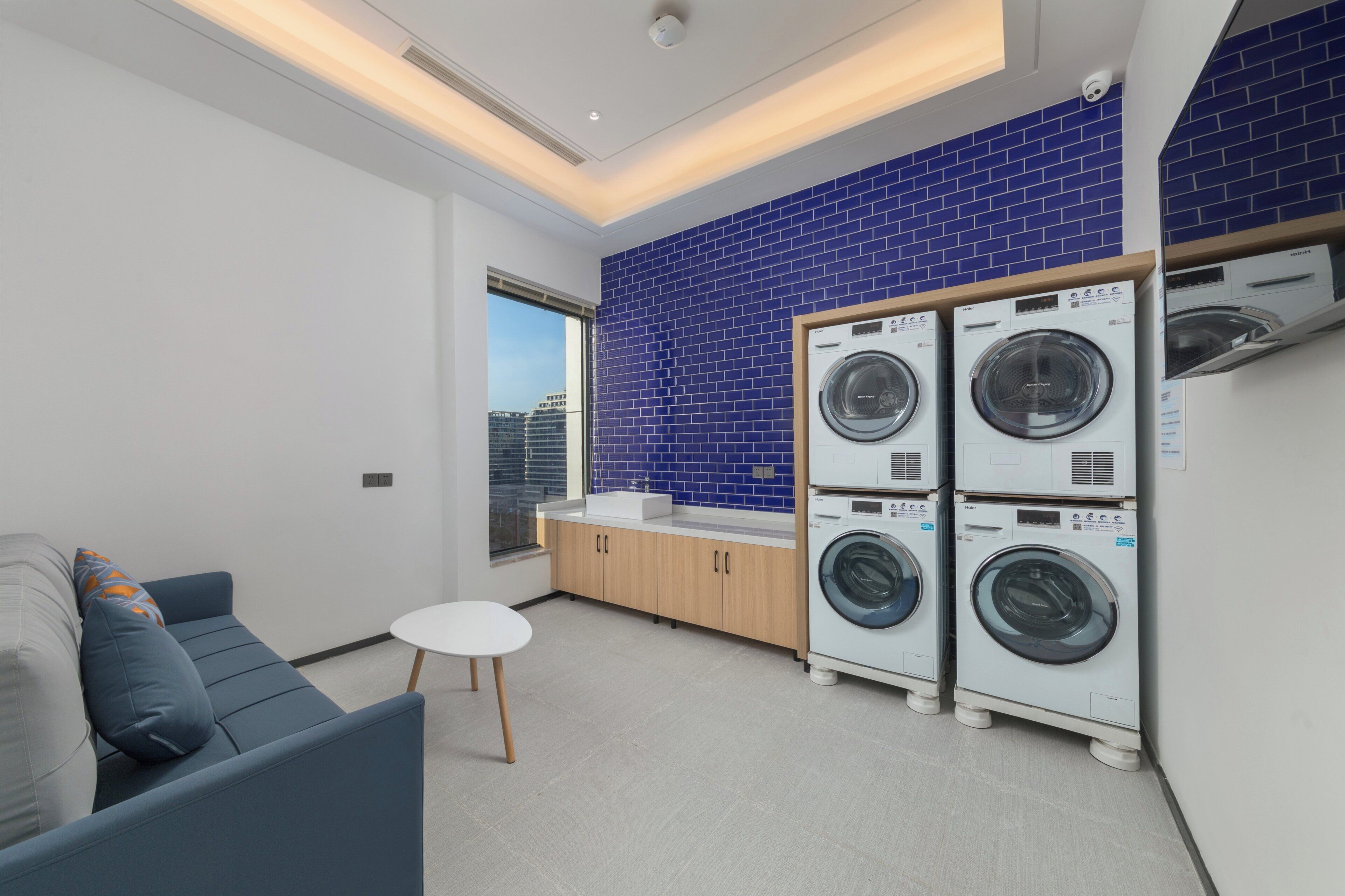 A modern laundry room with a blue-tiled wall, a white sink, and stacked front-loading washers.