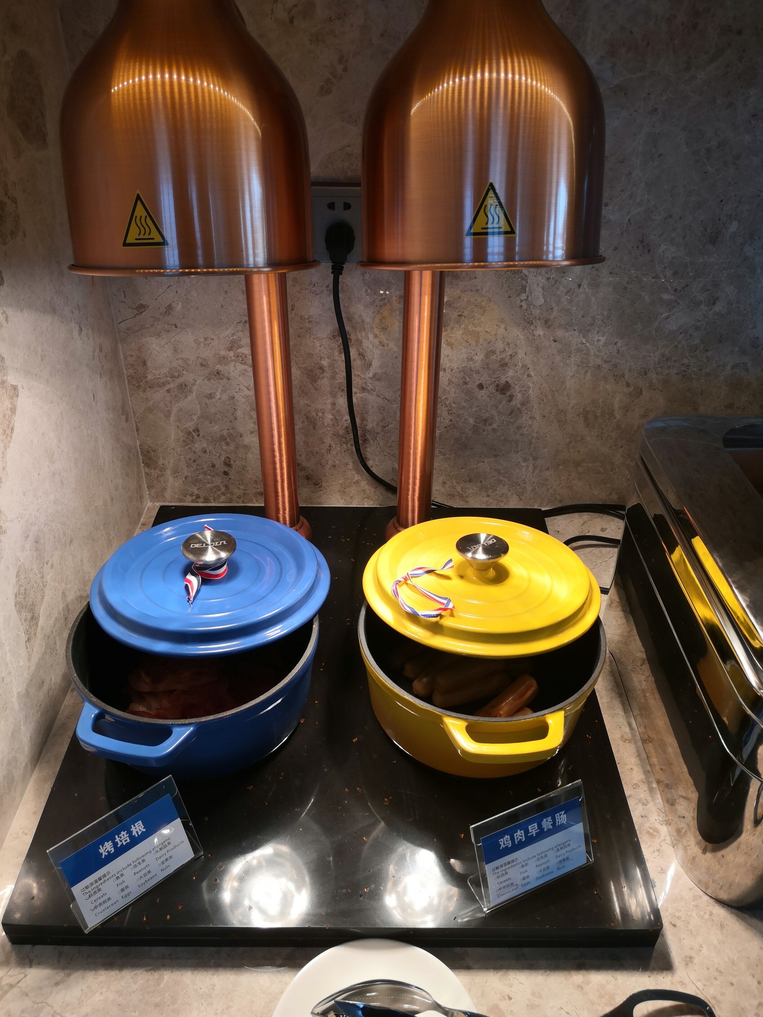 Un rincón de cocina con dos ollas sobre una estufa, cada una con una tapa de color diferente, y un letrero que indica el tipo de comida que se prepara.