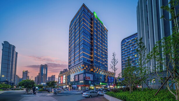 Un hotel moderno de gran altura con un llamativo letrero verde, rodeado de otros edificios altos y una calle concurrida.