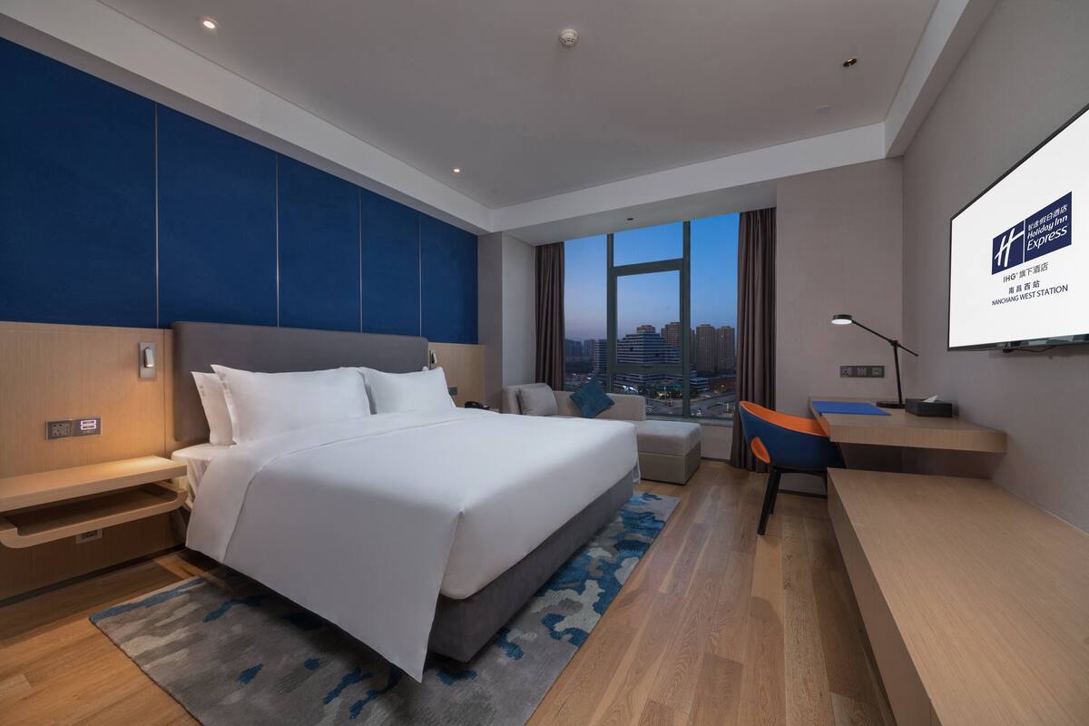 Une chambre d’hôtel moderne avec un grand lit, un bureau et une vue sur le paysage urbain.