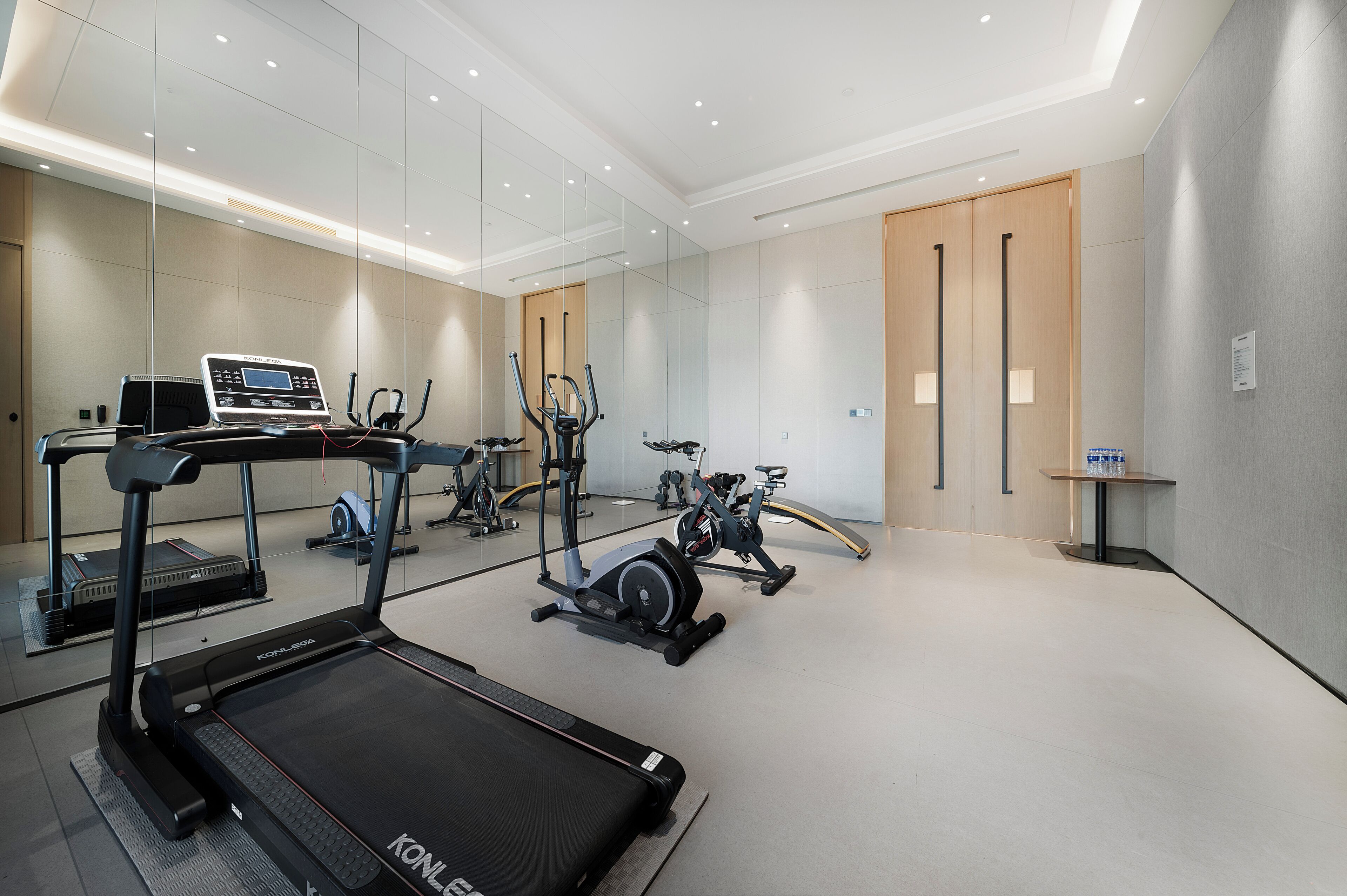 Un gimnasio moderno con equipo de cardio, incluyendo cintas de correr y bicicletas estáticas, y un espejo grande en la pared.