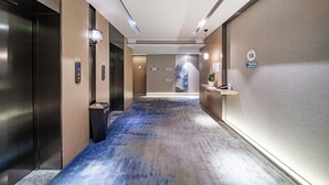 Un pasillo moderno de hotel con ascensores, una recepción y una alfombra azul.