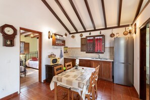 A kitchen with wooden cabinets, a stainless steel refrigerator, a dining table with chairs, and a clock on the wall.