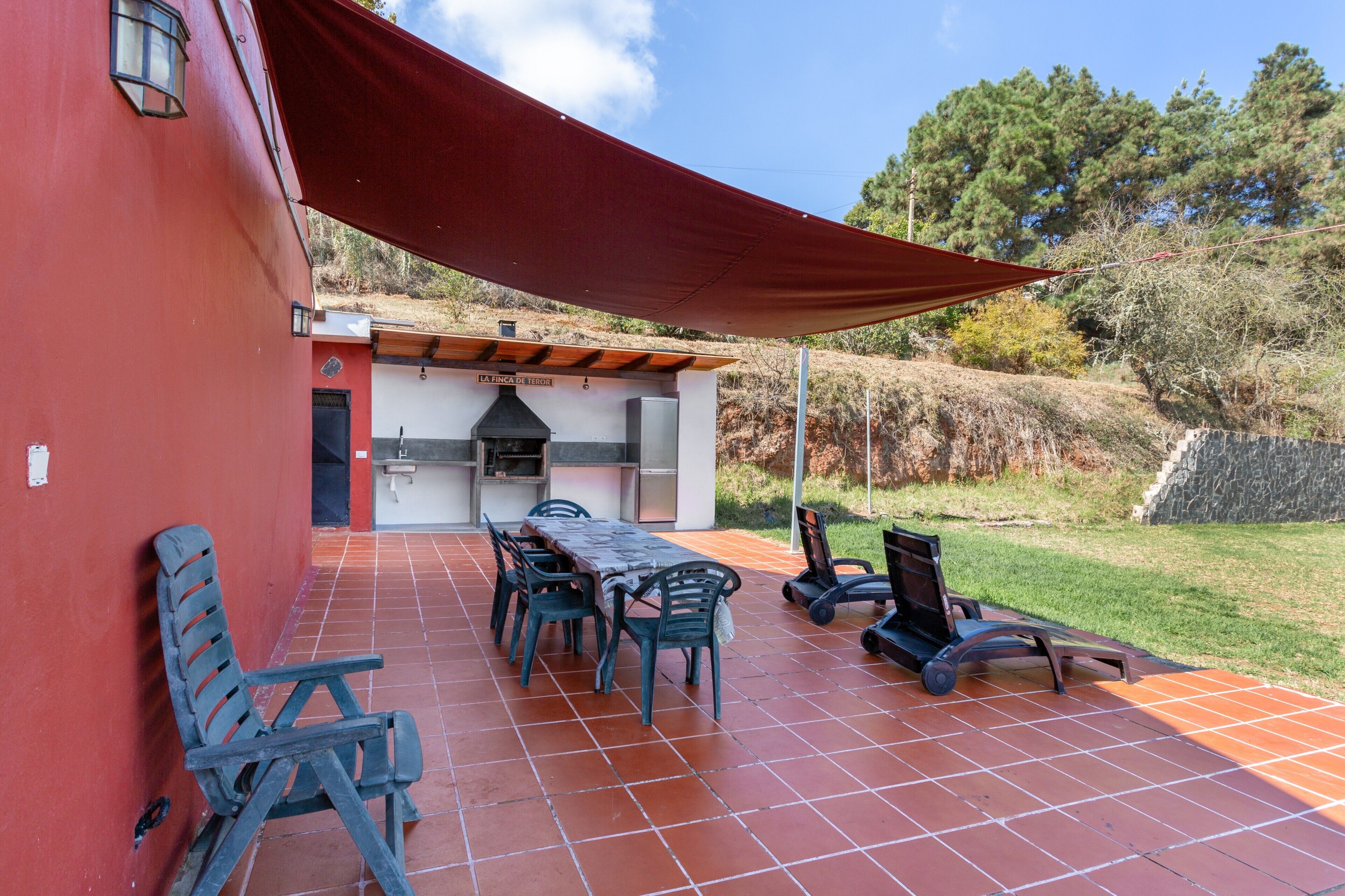 An outdoor patio with a table and chairs, a barbecue grill, and a red awning.