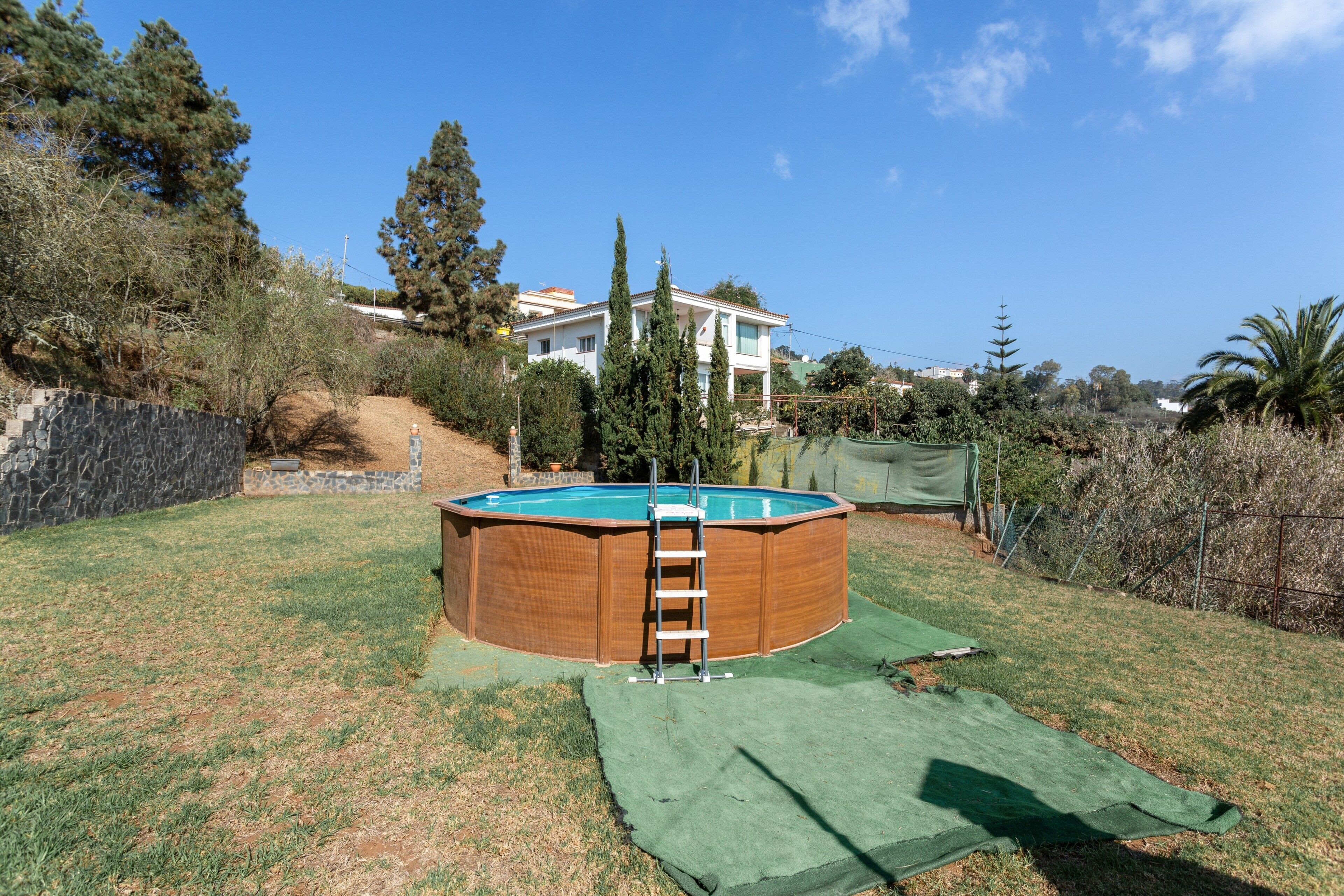 A backyard with a wooden swimming pool, a ladder, and a green tarp on the ground.