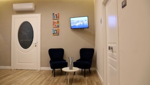 A room with a white door, two dark blue chairs, a small white table with a vase, a mounted TV, and a wall-mounted air conditioner. - Garibaldi Rooms (Naples)