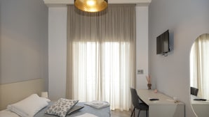 A modern hotel room with a bed, desk, chair, and large windows with curtains. - Garibaldi Rooms (Naples)