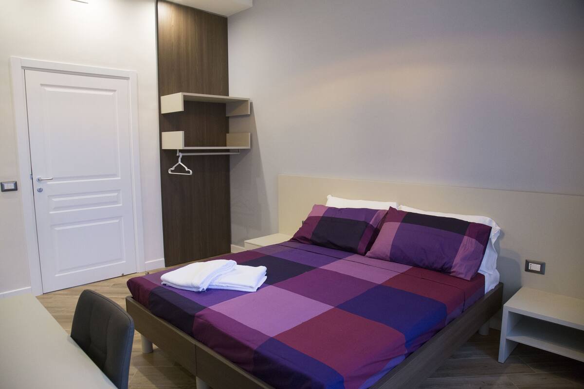 A bedroom with a bed, a bedside table, a chair, a wardrobe, and a door.