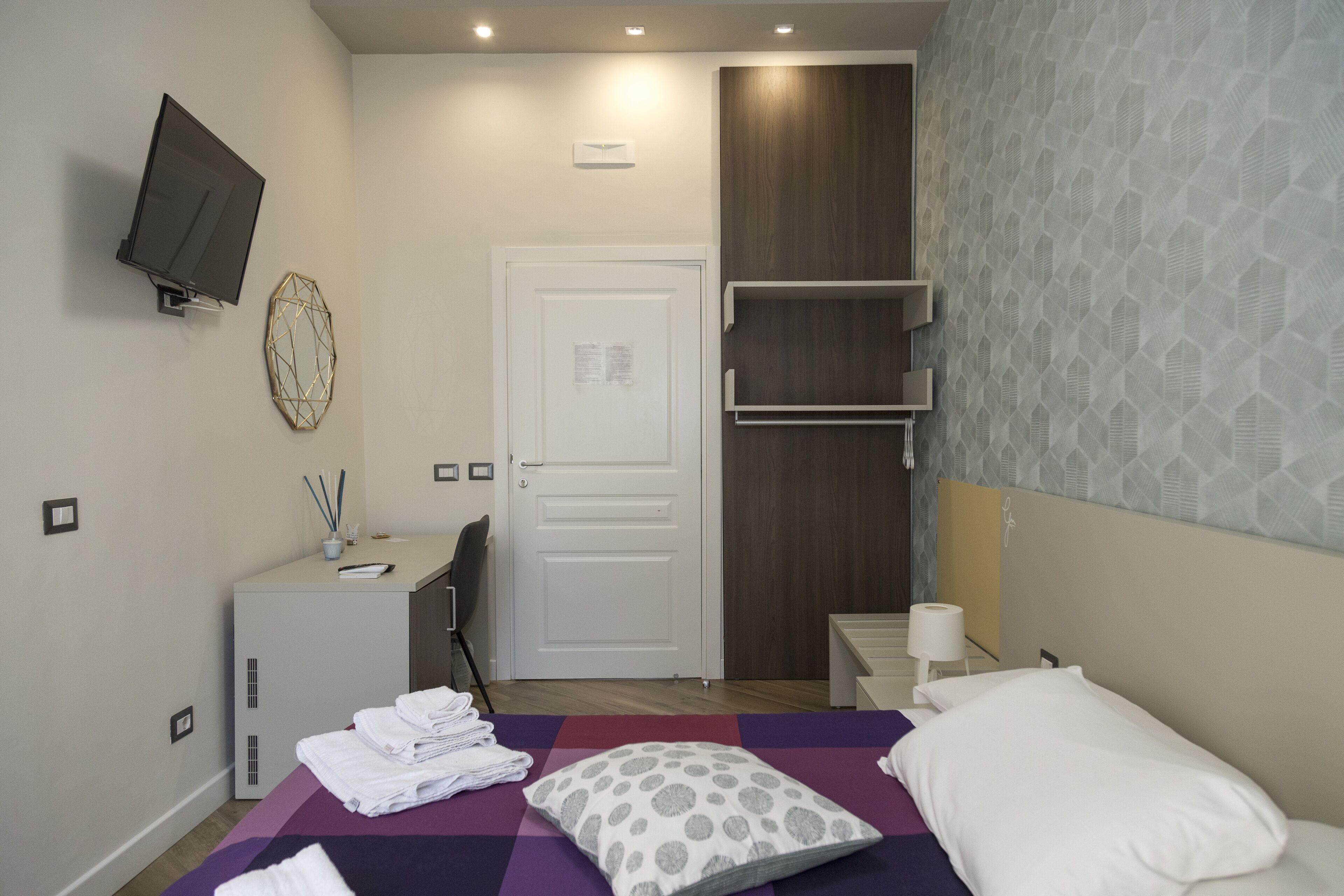 A modern hotel room with a bed, a desk, a TV, and a wardrobe.