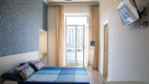 A bedroom with a bed, a TV mounted on the wall, and a view of the outside through a door. - Garibaldi Rooms (Naples)
