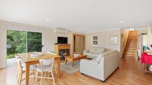 A spacious living room with a wooden dining table, white sofa, and a fireplace. - Sky Mirror Cottage - sleeps 9 (RHYLL)