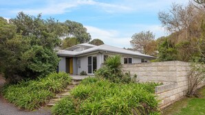 A modern two-story house with a stone retaining wall, surrounded by lush greenery and trees. - Sky Mirror Cottage - sleeps 9 (RHYLL)