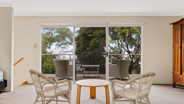 A balcony with wicker chairs and a small table, a wooden cabinet, and a view of trees and a bridge. - Sky Mirror Cottage - sleeps 9 (RHYLL)