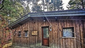 Une cabane en bois rustique, dotée d’une porte d’entrée, de deux fenêtres et d’un petit porche.