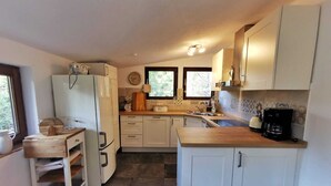 Une cuisine compacte avec des meubles blancs, un plan de travail en bois, un réfrigérateur, une machine à café et une fenêtre qui laisse entrer la lumière naturelle.