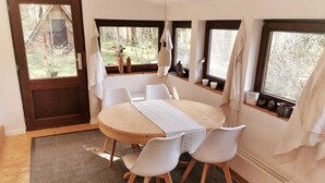Un espace repas comprenant une table ronde, des chaises blanches, un plancher en bois et des fenêtres avec des rideaux.