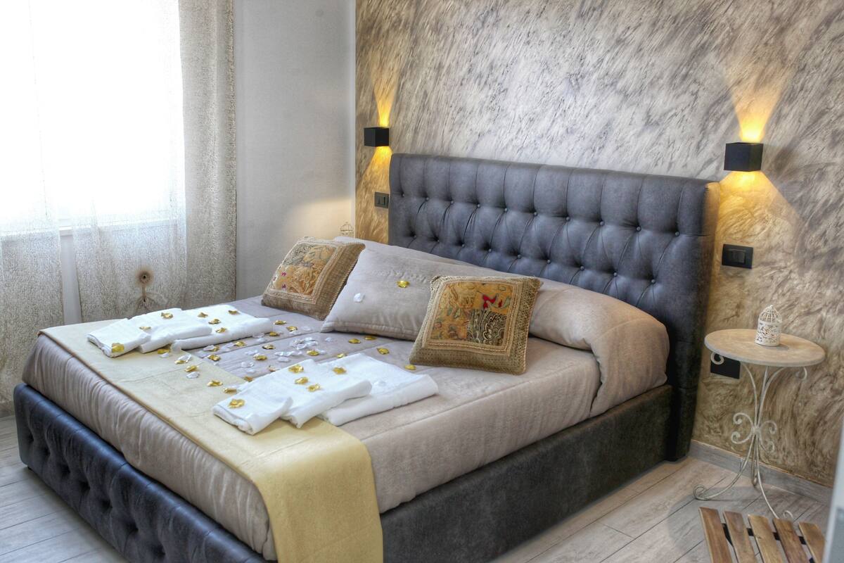 A neatly made bed with a grey headboard, two decorative pillows, and a bedside table with a small decorative item.