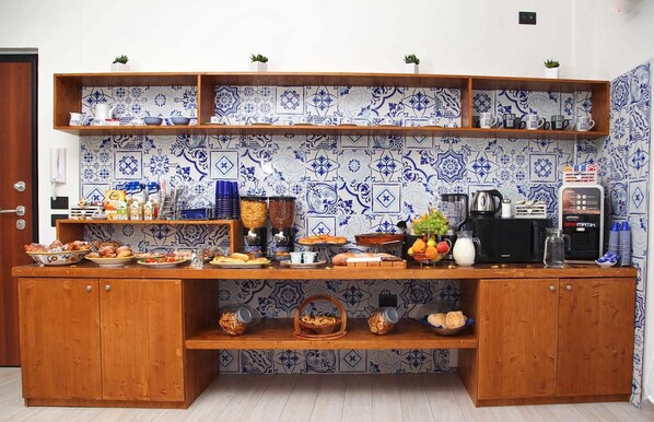 Una encimera de cocina con diversos alimentos, una máquina de café y una estantería con azulejos decorativos.