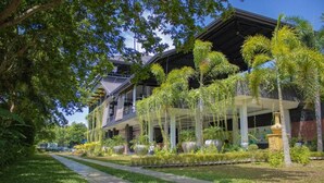 A modern building with a covered outdoor area, surrounded by lush greenery and palm trees. - Sigiriya Kingdom Resort (Dambulla)