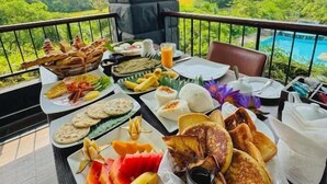 A table set with breakfast items and a view of lush greenery and mountains. - Sigiriya Kingdom Resort (Dambulla)
