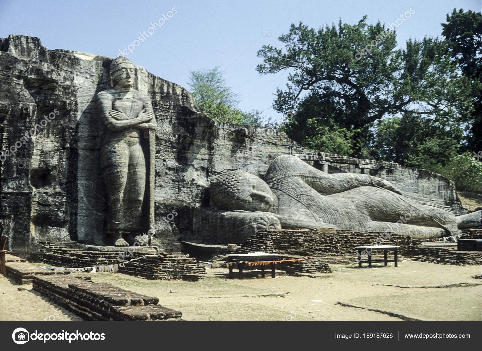Una gran estatua de Buda de piedra y una figura reclinada de Buda en un sitio histórico con escaleras y bancos de piedra.