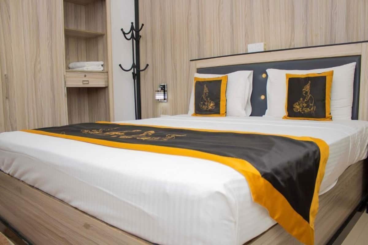 Uma cama bem arrumada com edredom preto e branco, cabeceira de madeira e mesa de cabeceira com luminária.