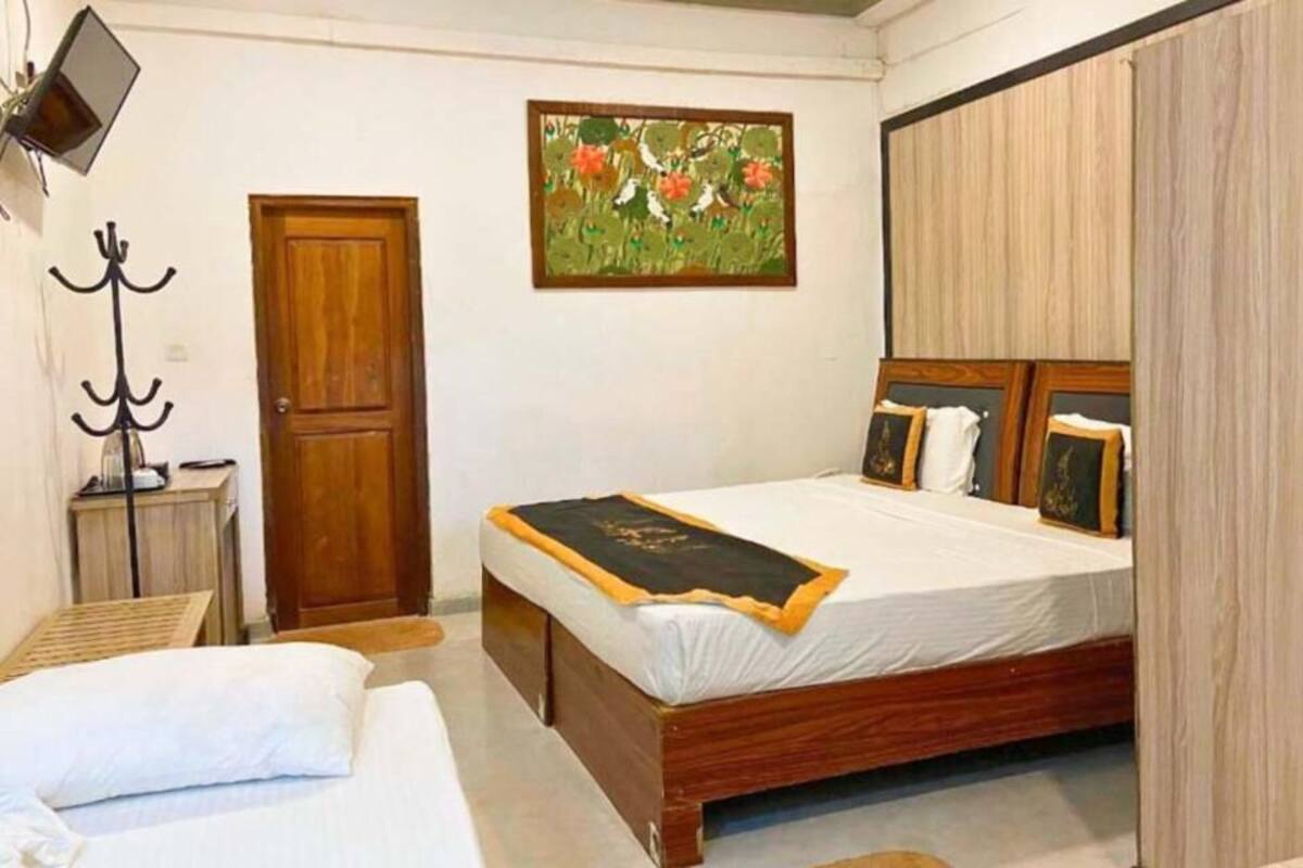 Quarto com cama de madeira, porta, cabideiro e um quadro na parede.