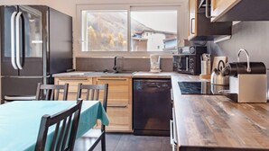 Eine moderne Küche mit Holztisch und -stühlen, einem Geschirrspüler, einem Kühlschrank und einem Fenster mit Blick auf die Berge.