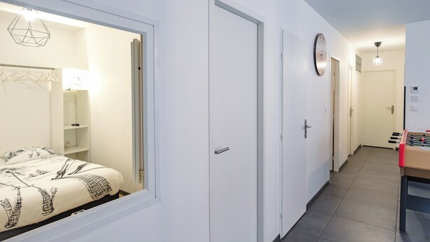 Ein Hotelkorridor mit einem Bett, einer Tür, einer Uhr und einem Kicker.