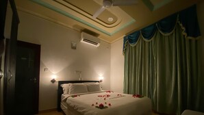 Habitación de hotel con cama, dos lámparas de noche, aire acondicionado, ventilador de techo y ventana con cortinas.