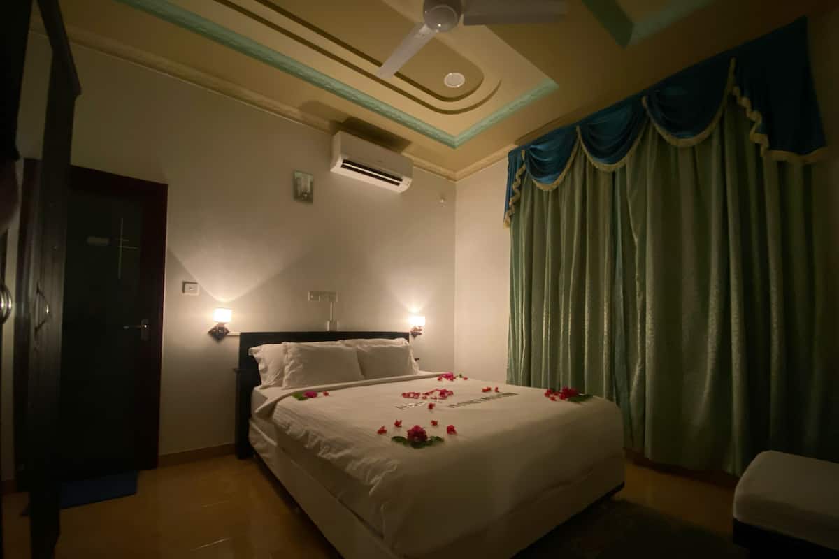 Une chambre d’hôtel comprenant un lit, deux lampes de chevet, un appareil de climatisation, un ventilateur de plafond et une fenêtre avec des rideaux.