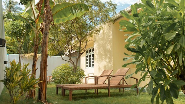 Un jardín con una silla de mimbre, una mesita y una pared blanca con una ventana.