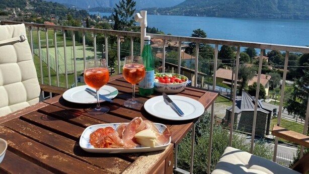 A balcony with a table set for a meal, a bottle of water, a glass of red wine, and a plate of food. - Como Lake view from olive garden, balcony and pool (Tremezzina)