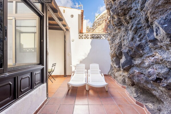 A patio with two white lounge chairs, a door, and a stone wall.