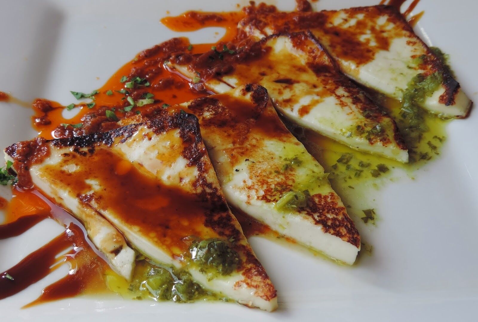 A white plate with grilled fish fillets, green sauce, and a red sauce.