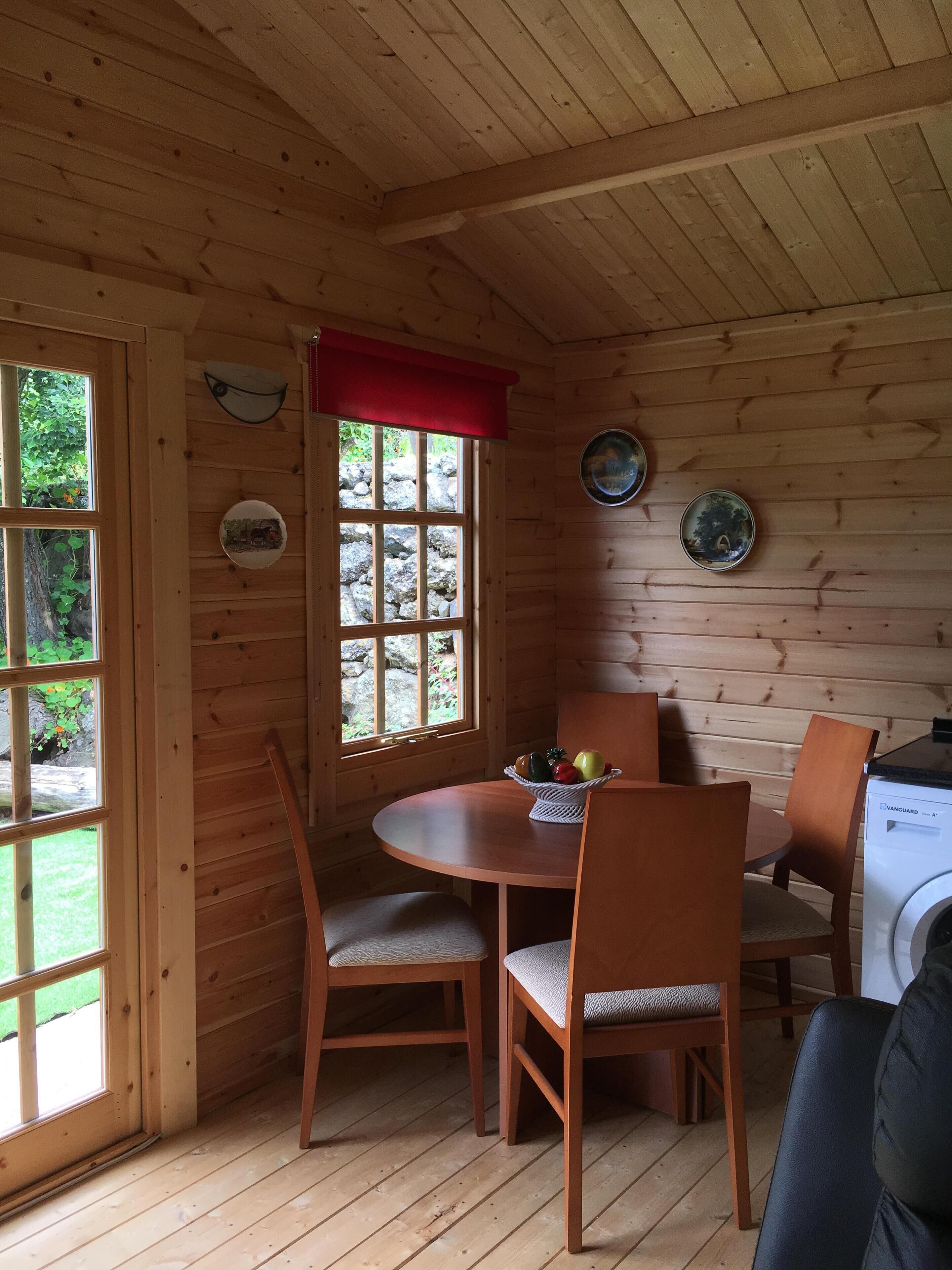 L’intérieur d’un chalet en bois comprend une table à manger, des chaises, une fenêtre agrémentée d’un rideau rouge et un lave-linge.