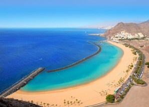 A coastal beach with a clear blue sea, a sandy shore, and a rocky breakwater.