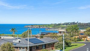 A coastal residential area with a house featuring solar panels, a view of the ocean, and a golf course in the background. - 45 Hillside Cres Beach House (Kianga)