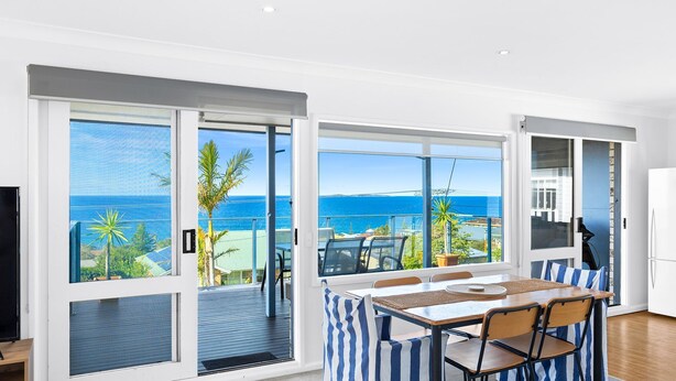 A modern room with a large sliding glass door leading to a balcony with a view of the sea. - 45 Hillside Cres Beach House (Kianga)