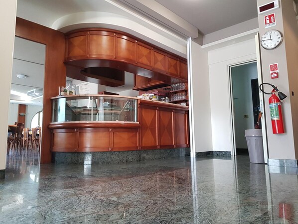 A hotel lobby with a marble floor, wooden reception desk, and a fire extinguisher on the wall.