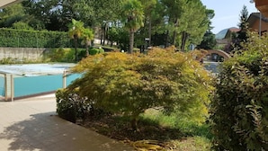A swimming pool with a tiled deck, surrounded by lush greenery and trees. - Hotel Rio re (Acquaviva)