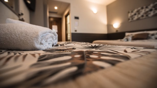 A hotel room with a neatly made bed, a visible door leading to another room, and a wall-mounted light fixture. - Hotel Rio re (Acquaviva)