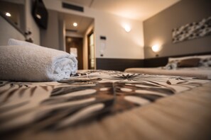 A hotel room with a neatly made bed, a visible door leading to another room, and a wall-mounted light fixture.