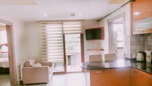 Una cocina moderna con una televisión de pantalla plana, una zona de comedor con mesa y sillas, y un ventanal corredero que da a un balcón.