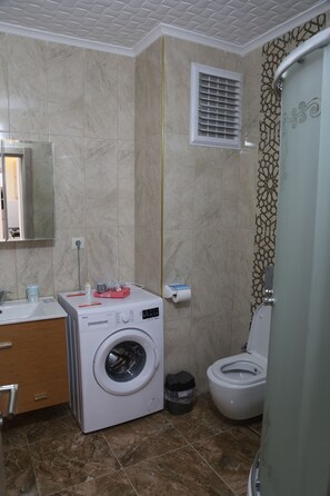 Een badkamer met een wasmachine, toilet en een douchehoek.
