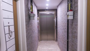 Un pasillo con suelo de mármol, una puerta a la izquierda y un ascensor al final.