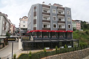 Een meerlaags gebouw met een café genaamd "HERA" op de begane grond, met terraszitplaatsen en een stenen muur.