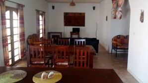 Una sala de estar con una mesa de comedor, sillas, un sofá, un ventilador de techo y un televisor.