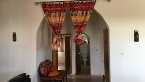 Habitación con sofá, una silla y un banco de madera. Dos puertas conducen a otras habitaciones.